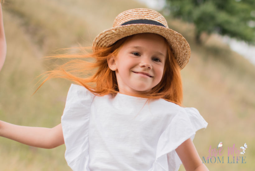 Cute red-headed girl with straw hat  and white dress on in field.