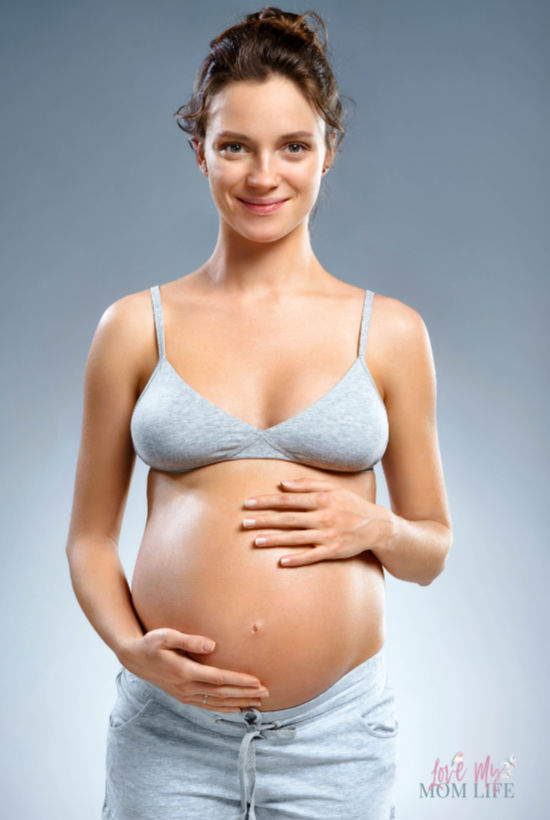 brown haired pregnant woman in gray bra and gray shorts smiling at camera